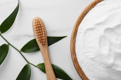 Bamboo toothbrush, green leaf and bowl of baking soda on white marble table, flat lay