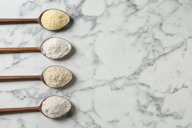 Spoons with different types of flour on marble background, top view. Space for text