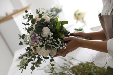 Photo of Florist holding beautiful wedding bouquet at white table, closeup