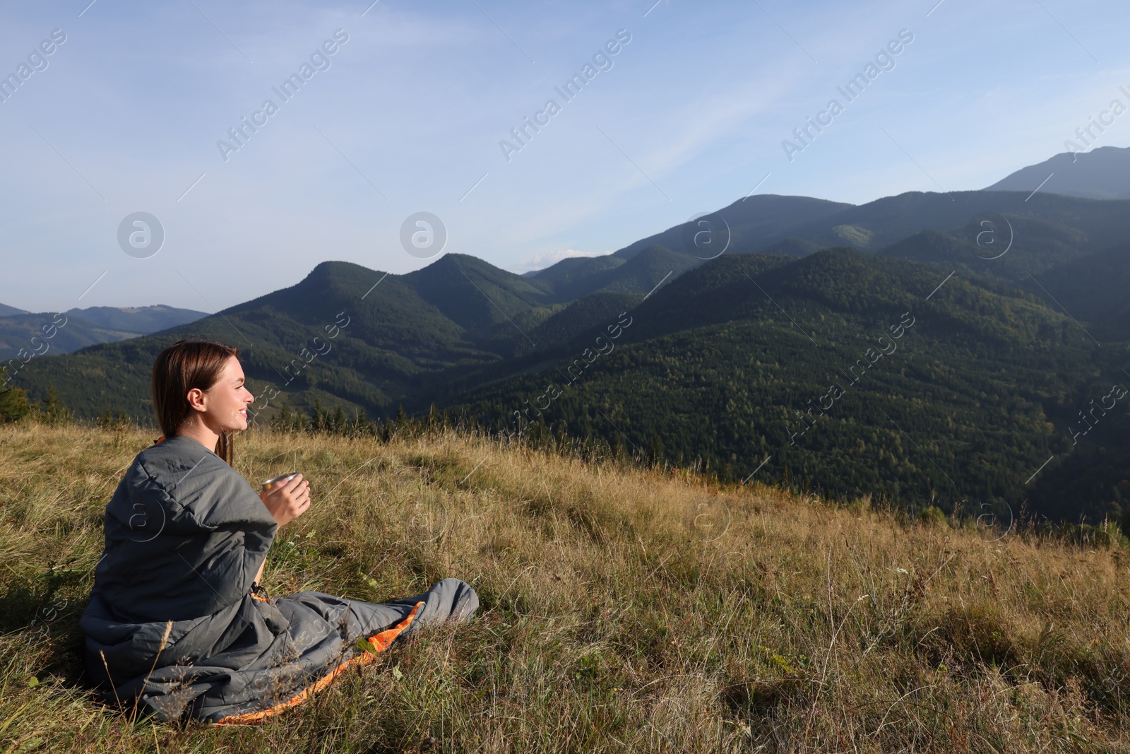 Photo of Young woman with drink in sleeping bag surrounded by beautiful nature