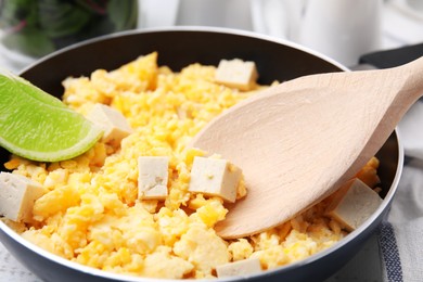 Taking delicious scrambled eggs and tofu with spoon from frying pan, closeup