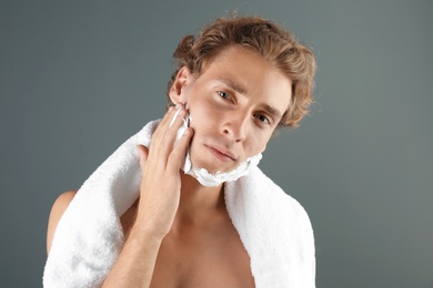 Young man applying shaving foam on gray background