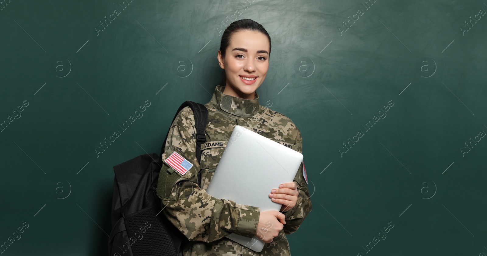 Image of Military education. Cadet with backpack and laptop near green chalkboard