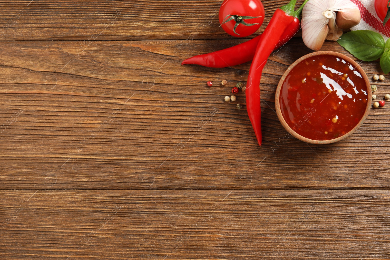 Photo of Spicy chili sauce and ingredients on wooden table, flat lay. Space for text