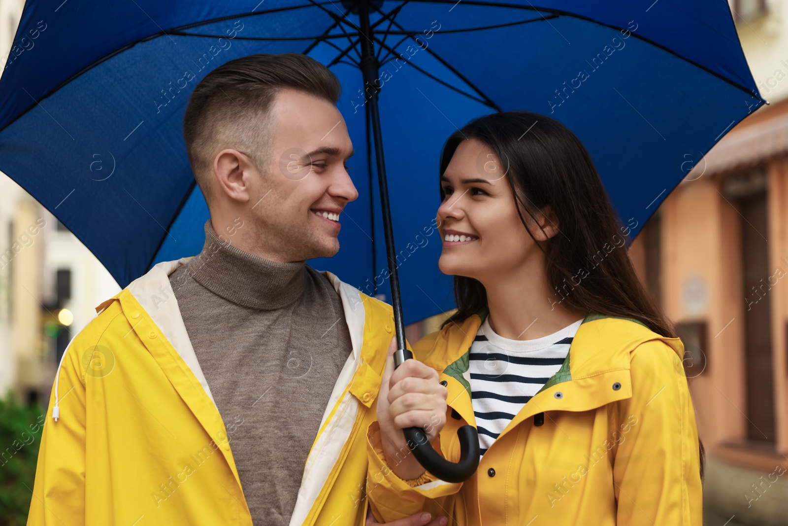 Photo of Lovely young couple with umbrella walking under rain on city street