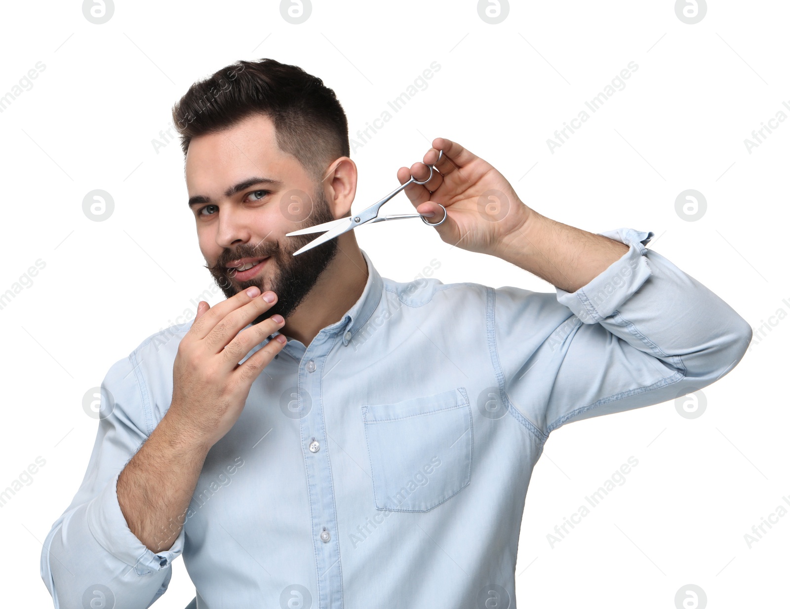 Photo of Handsome young man trimming beard with scissors on white background