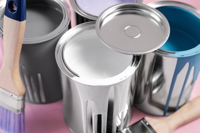 Photo of Cans of paints and brushes on pink background, closeup