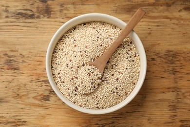 Photo of Raw quinoa seeds and spoon in bowl on wooden table, top view