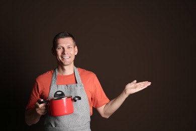 Photo of Happy man with cooking pot on brown background. Space for text