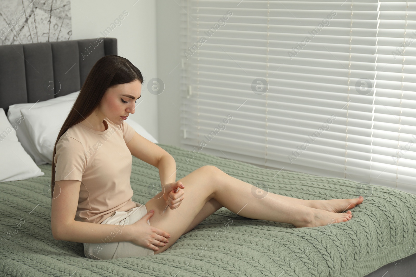 Photo of Diabetes. Woman making insulin injection into her leg on bed in room