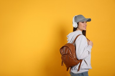 Photo of Beautiful young woman with stylish leather backpack and headphones on yellow background. Space for text