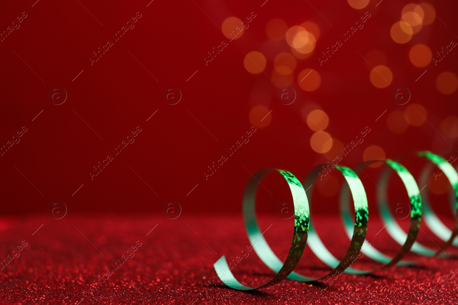 Photo of Shiny green serpentine streamer on red table against blurred lights, closeup. Space for text