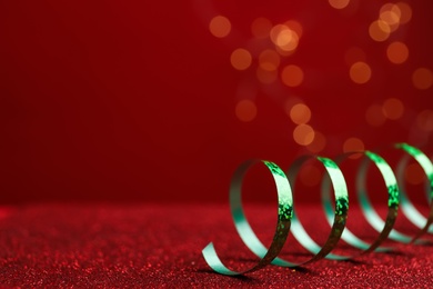 Shiny green serpentine streamer on red table against blurred lights, closeup. Space for text