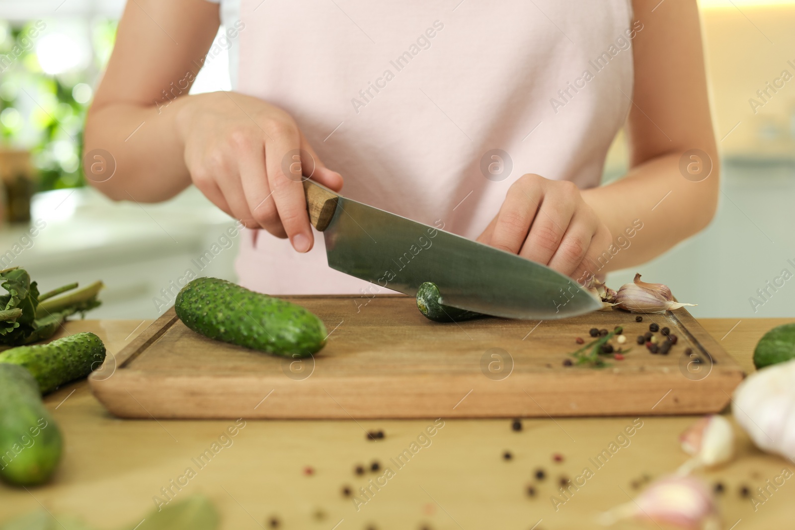 Photo of Woman cutting cucumber at table in kitchen, closeup