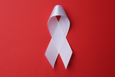 Photo of White awareness ribbon on red background, top view