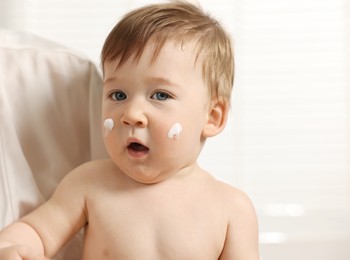 Mother holding her baby with body cream on face indoors