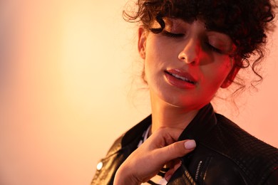 Beautiful young woman in black leather jacket posing on color background in neon lights, closeup. Space for text