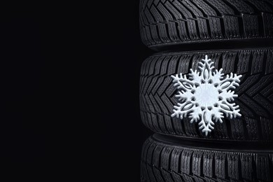 Image of Stacked winter tires with snowflake on black background, closeup. Space for text