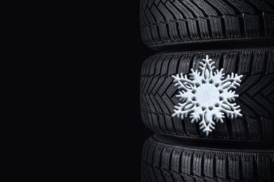 Stacked winter tires with snowflake on black background, closeup. Space for text