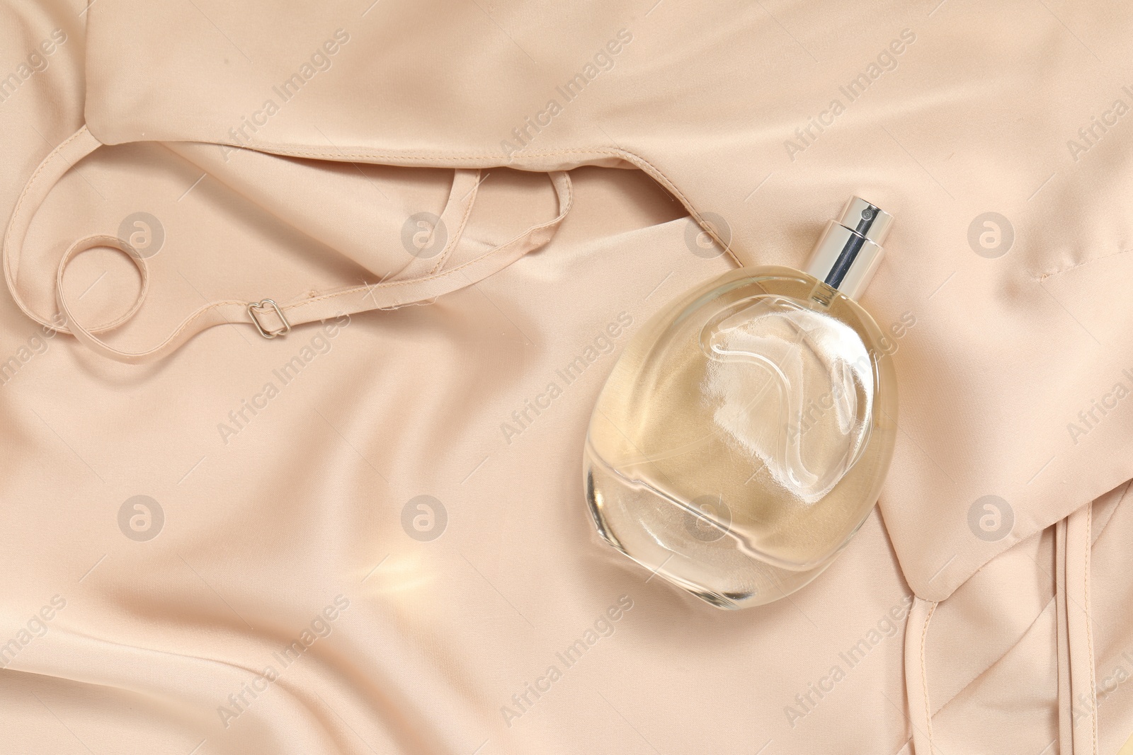 Photo of Luxury perfume in bottle on beige silk fabric, top view