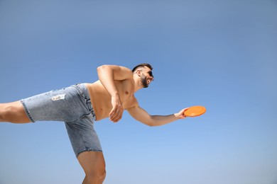 Photo of Happy man catching flying disk against blue sky on sunny day, low angle view