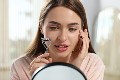Woman with eyelash curler near mirror indoors