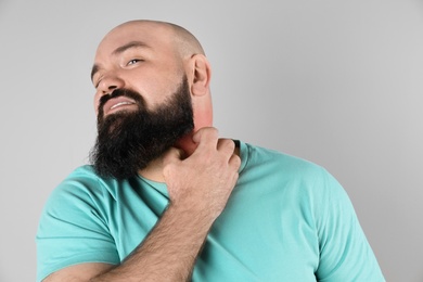 Photo of Man with allergy symptoms scratching neck on grey background