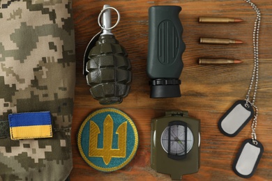 Photo of MYKOLAIV, UKRAINE - SEPTEMBER 26, 2020: Tactical gear and Ukrainian army patches on wooden table, flat lay