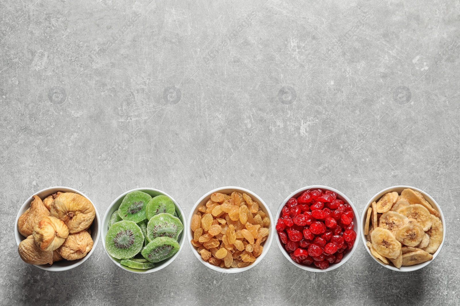 Photo of Bowls of different dried fruits on grey background, top view with space for text. Healthy food