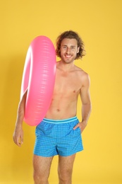 Attractive young man in beachwear with pink inflatable ring on yellow background
