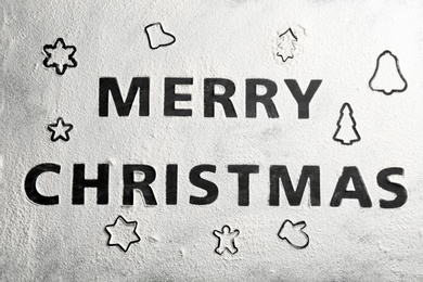 Photo of Different cookie shapes and phrase Merry Christmas made of flour on black table, top view