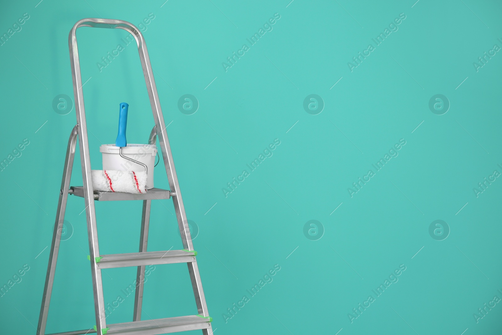 Photo of Bucket with paint and roller on step ladder near color wall