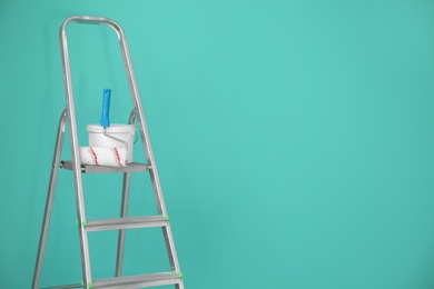 Photo of Bucket with paint and roller on step ladder near color wall