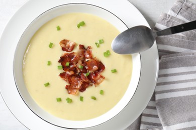 Photo of Tasty potato soup with bacon in bowl and spoon on white table, flat lay