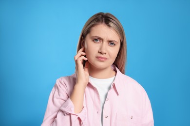 Young woman suffering from ear pain on light blue background