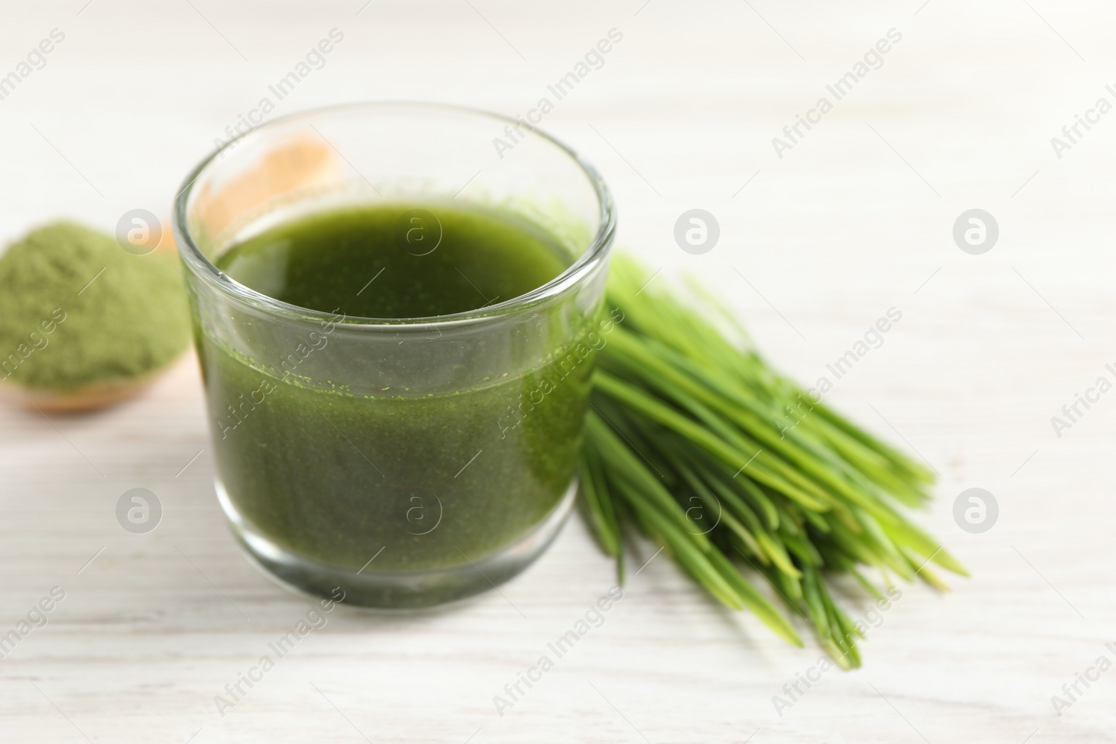 Photo of Wheat grass drink in glass and fresh sprouts on white wooden table, closeup