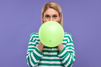 Woman blowing up balloon on violet background