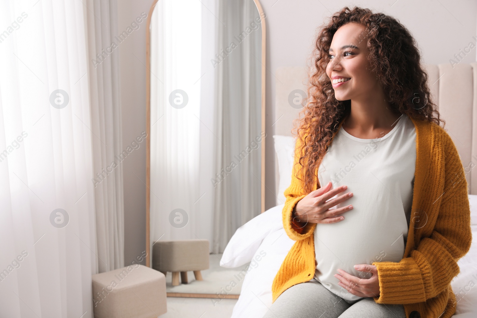 Photo of Pregnant young African-American woman sitting on bed at home