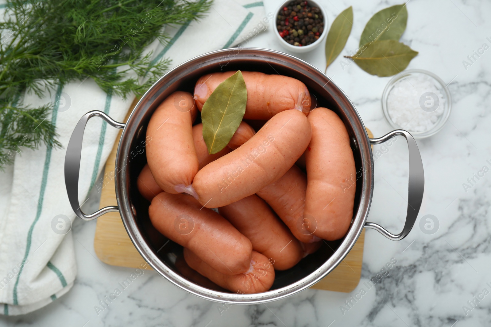 Photo of Pan of delicious sausages, dill, bay leaf, pepper and salt on white marble table, flat lay