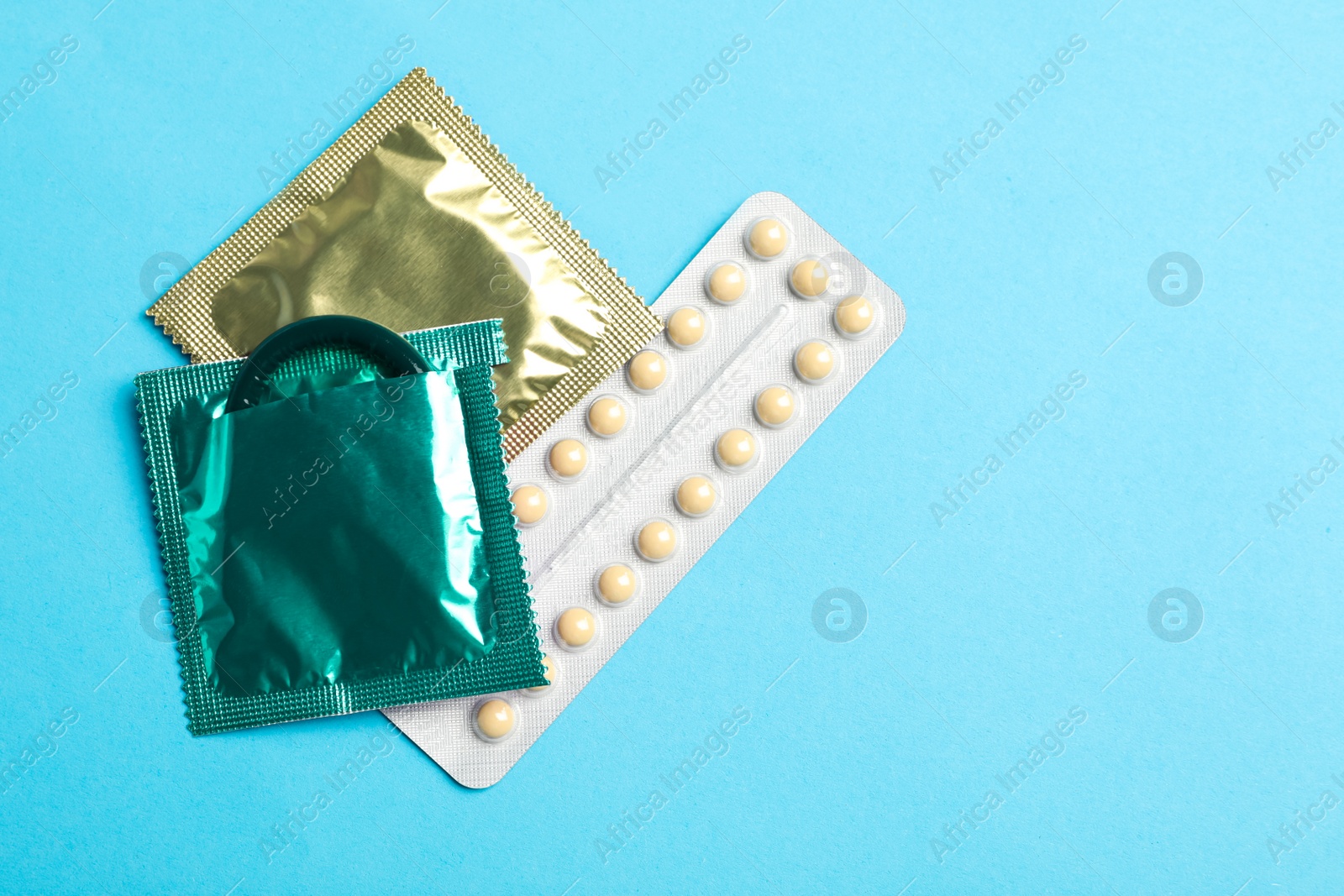 Photo of Condoms and birth control pills on light blue background, flat lay with space for text. Safe sex concept