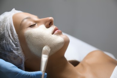 Cosmetologist applying mask on client's face in spa salon