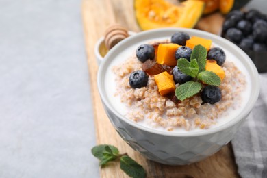 Tasty wheat porridge with pumpkin, dates and blueberries in bowl on light gray table, closeup. Space for text