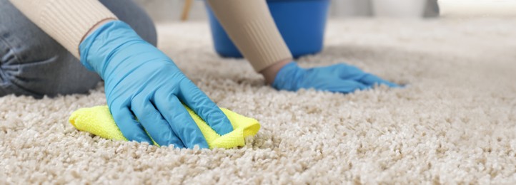 Image of Woman in rubber gloves cleaning carpet with rag indoors, closeup. Banner design