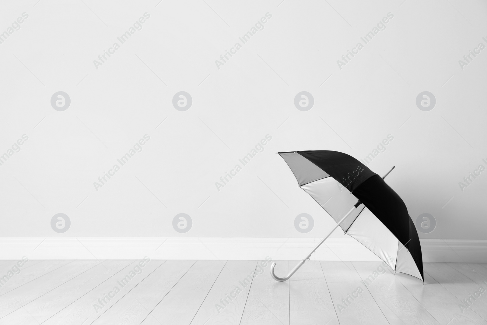 Photo of Beautiful open umbrella on floor near white wall with space for design