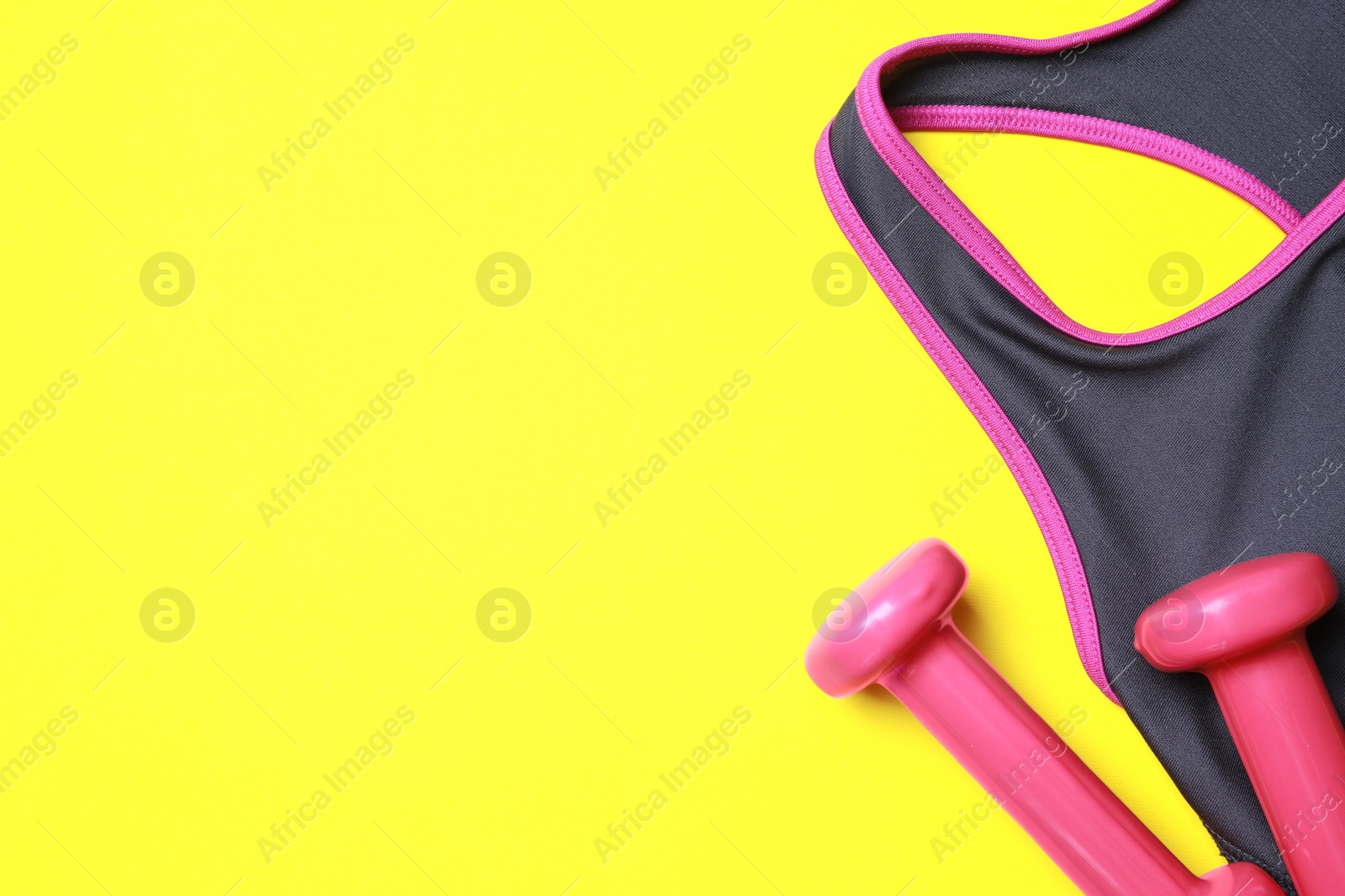 Photo of Stylish sports bra and dumbbells on yellow background, flat lay. Space for text