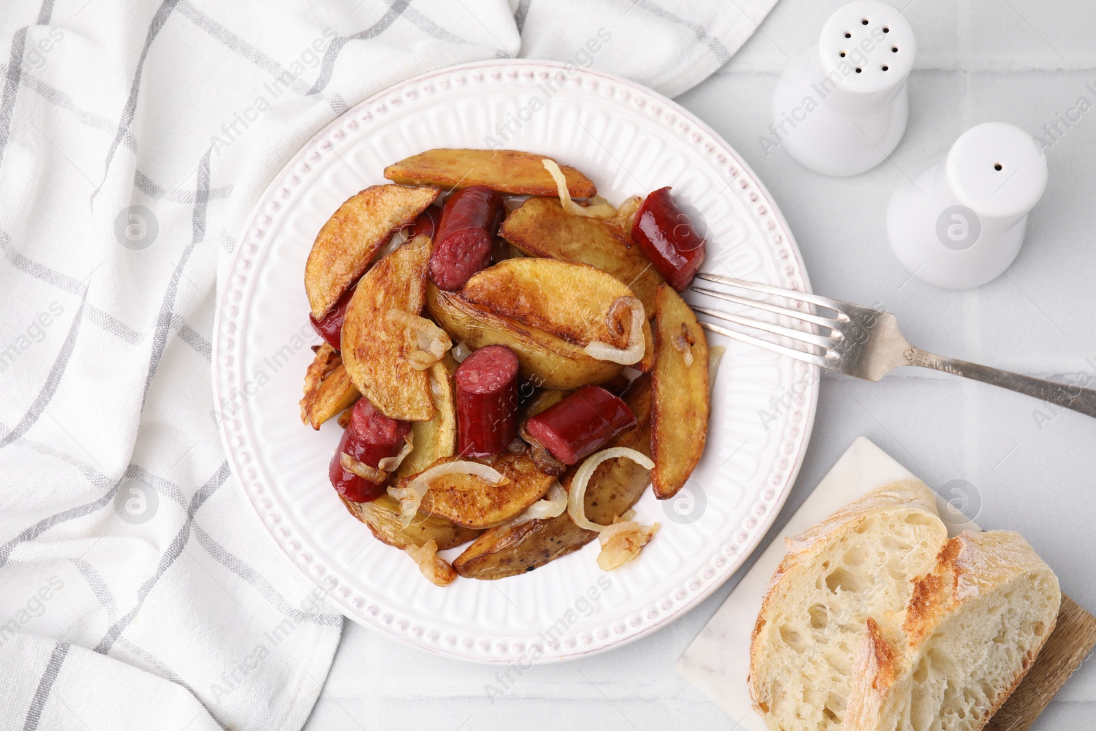 Photo of Delicious baked potato with thin dry smoked sausages and onion served on white tiled table, flat lay