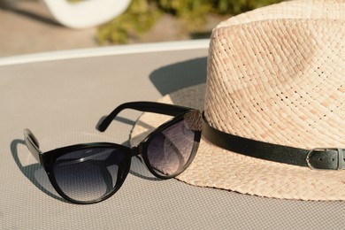 Stylish hat and sunglasses on grey sunbed outdoors, closeup