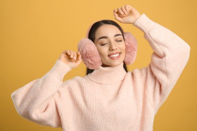 Beautiful young woman wearing earmuffs on yellow background