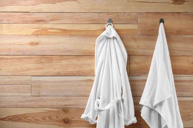 Photo of Soft comfortable bathrobe and towel hanging on wooden wall. Space for text