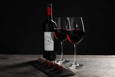 Photo of Red wine and chocolate truffles on gray table against dark background